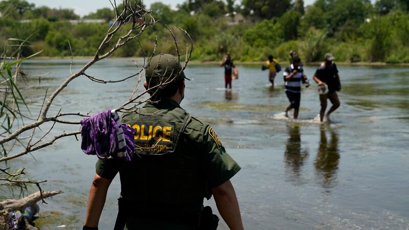 In this June 15, 2021, file photo, a Border Patrol agent watches as a group of migrants walk...